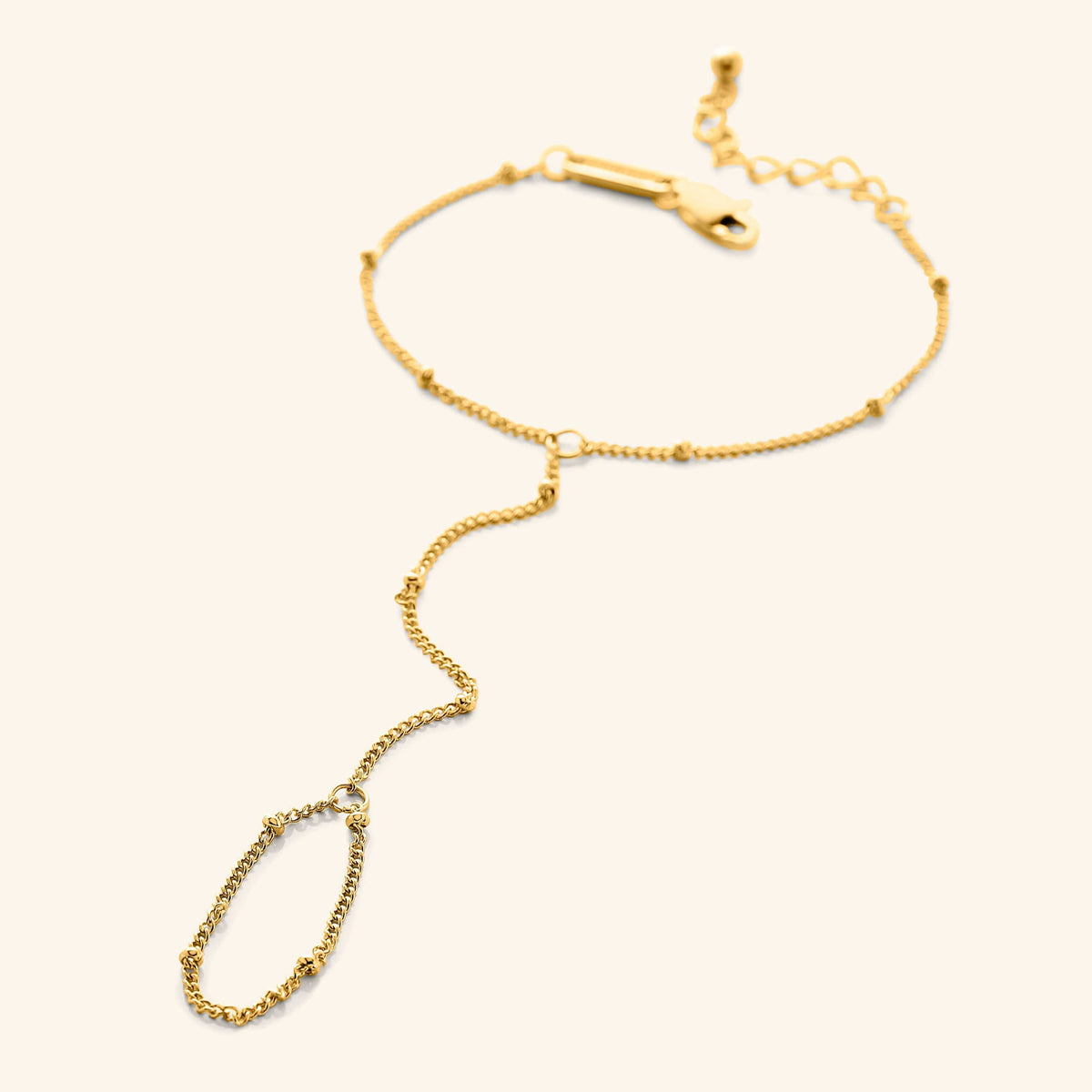Flat lay of a gold dotted hand chain with a slim bracelet attached to a matching finger loop by a fine chain.
