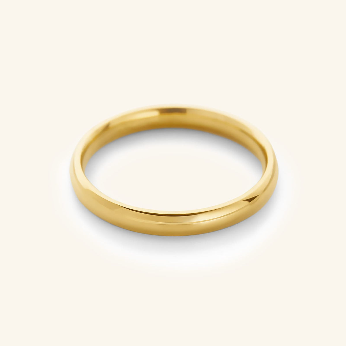 A minimalist, highly polished 18k gold-plated classic band ring resting on a soft cream background.
