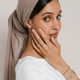 Model wearing 18k gold-plated jewelry featuring a ring stack with the Mughal Bloom Bezel Ring on the index finger, Intertwined Bezel Ring on the middle finger, and North Star Bezel Ring on the ring finger, paired with a Bezel Stud earring, layered gold necklaces, and a wrist stack featuring the Tennis Name Bracelet with custom Arabic calligraphy.