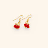 The Pomegranate Vine Earrings by Nominal, featuring rich red pomegranate charms hanging from delicate 18k gold-plated vine and leaf accents on fishhook wires, displayed on an off-white background.