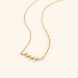The Pavé Olive Branch Necklace by Nominal, featuring a delicate 18k gold-plated chain with a curved horizontal olive branch pendant set with sparkling marquise crystals, displayed on an off-white background.