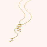 The Pavé Olive Branch Lariat Necklace by Nominal, featuring a delicate 18k gold-plated chain joined by a central ring with asymmetrical sparkling crystal olive leaf drops, displayed on an off-white background.