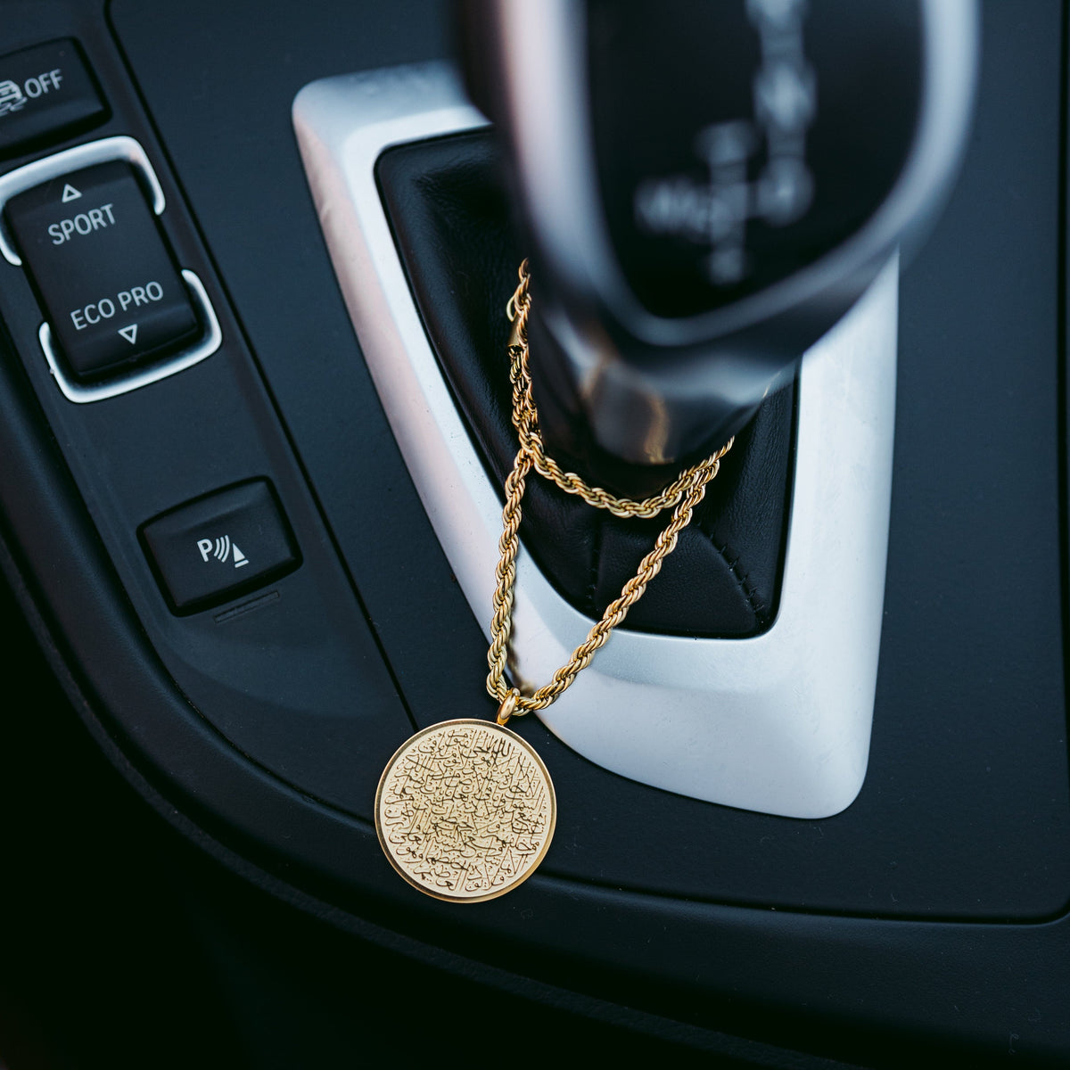 Close up of the gold Ayatul Kursi Car Hanger on a car gear stick.