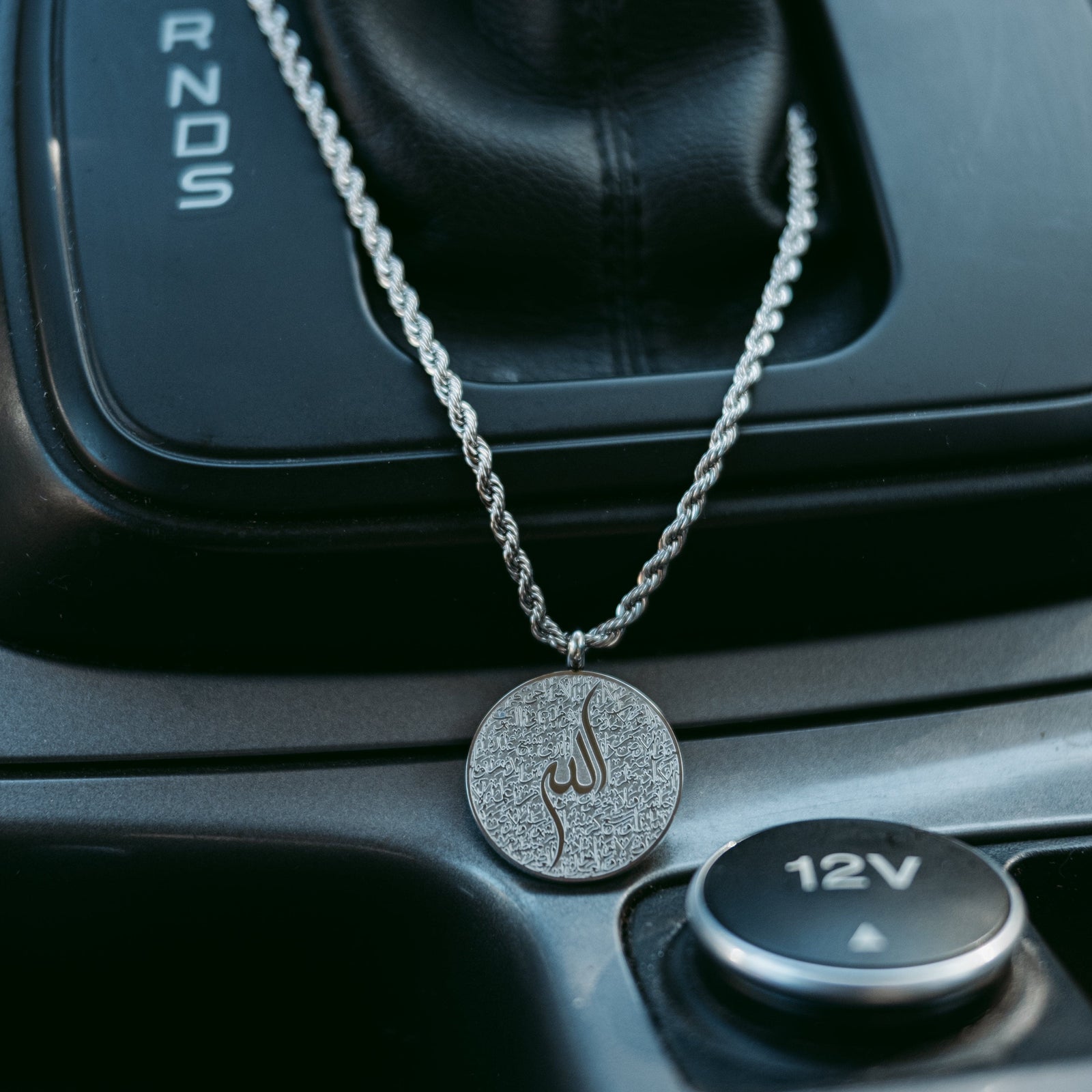 Silver Ayatul Kursi car hanger draped on a car gear shift, pendant resting on the console.