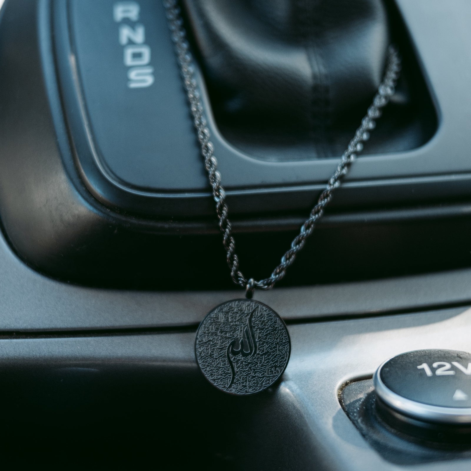Black Ayatul Kursi car hanger resting beside a car gear shift.