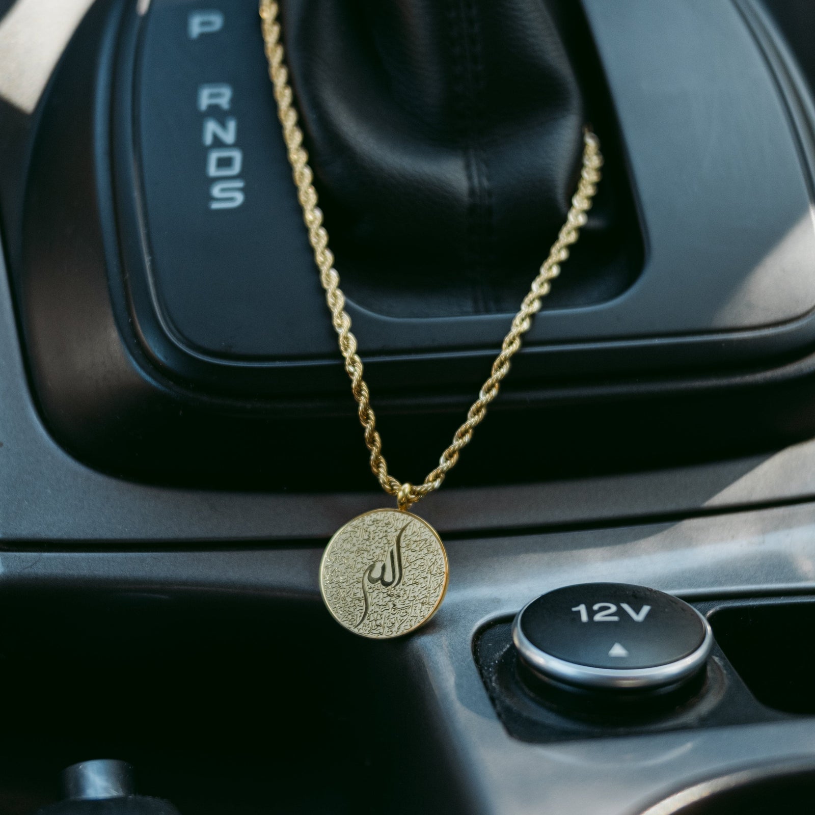 Gold Ayatul Kursi car hanger with the pendant laying flat against the console.