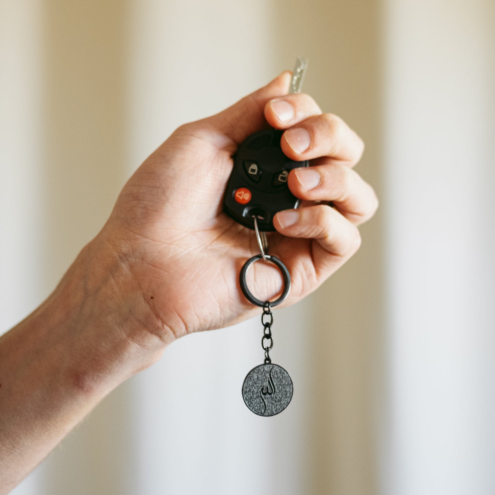 Model holds a car key to show the black Ayatul Kursi Keychain V2 linked to it. 