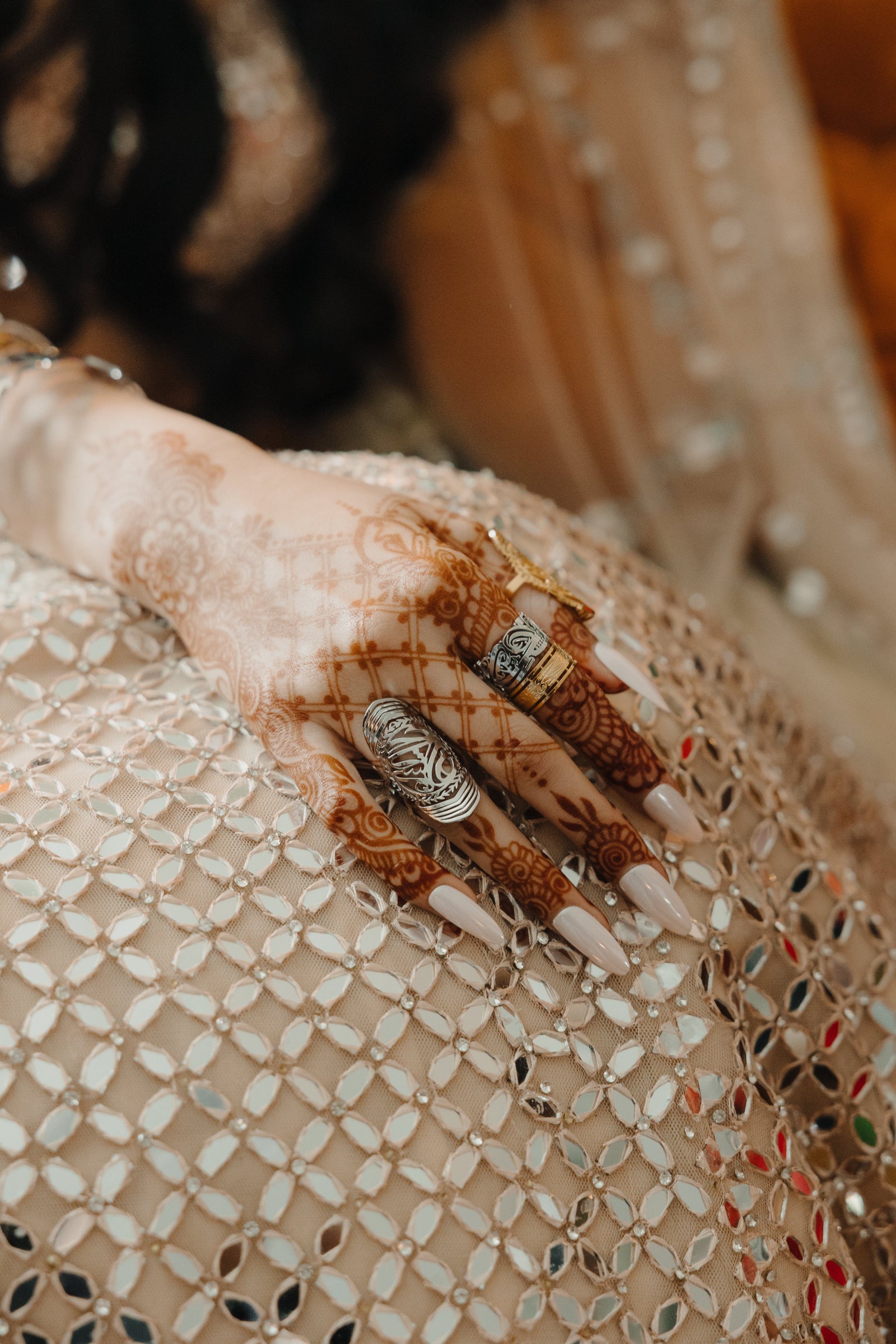 Woman with henna-adorned hand wearing the gold Sufficient Ring among stacked gold bangles and patterned attire.