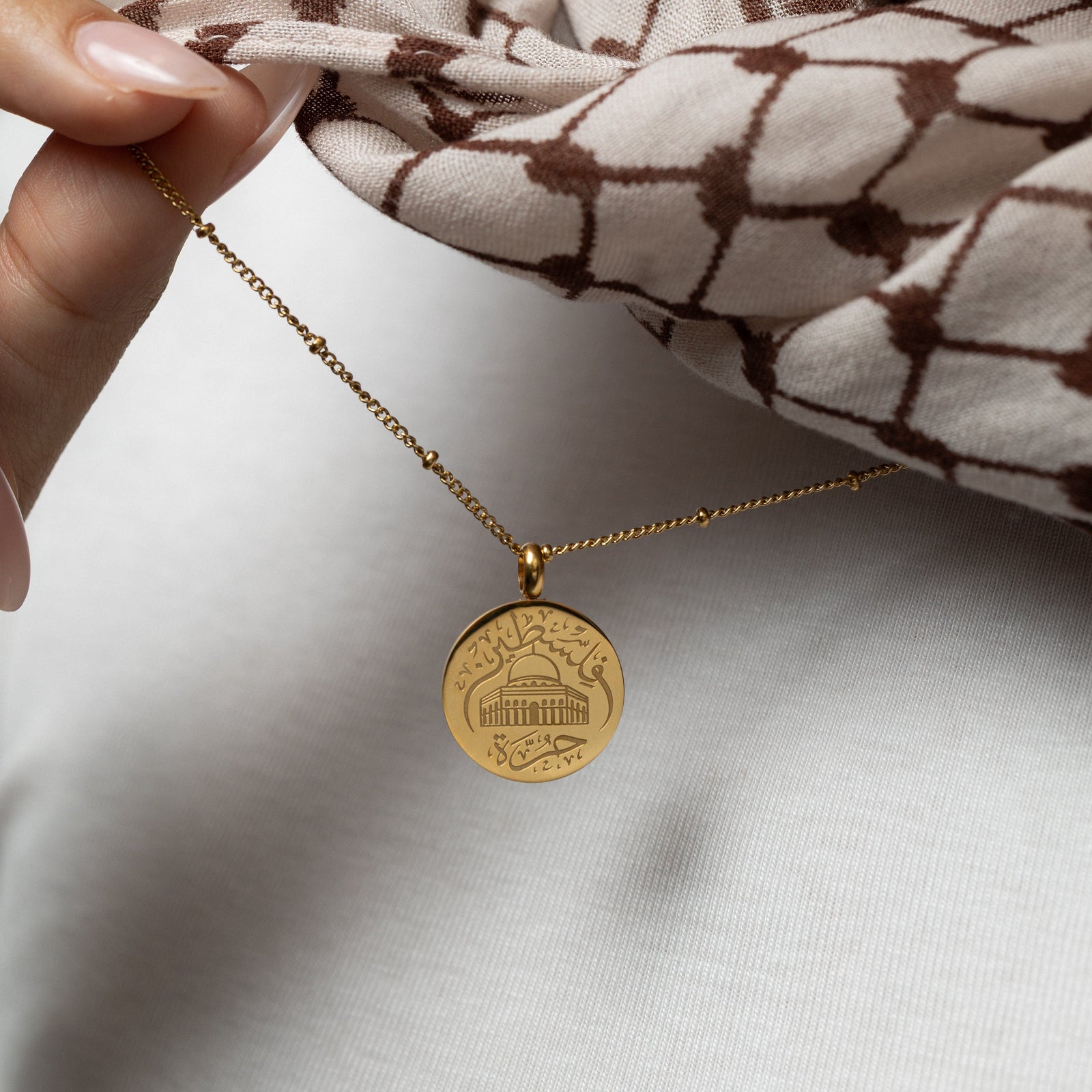 Gold Al-Aqsa ‘Free Palestine’ Necklace held by a hand against a white fabric background