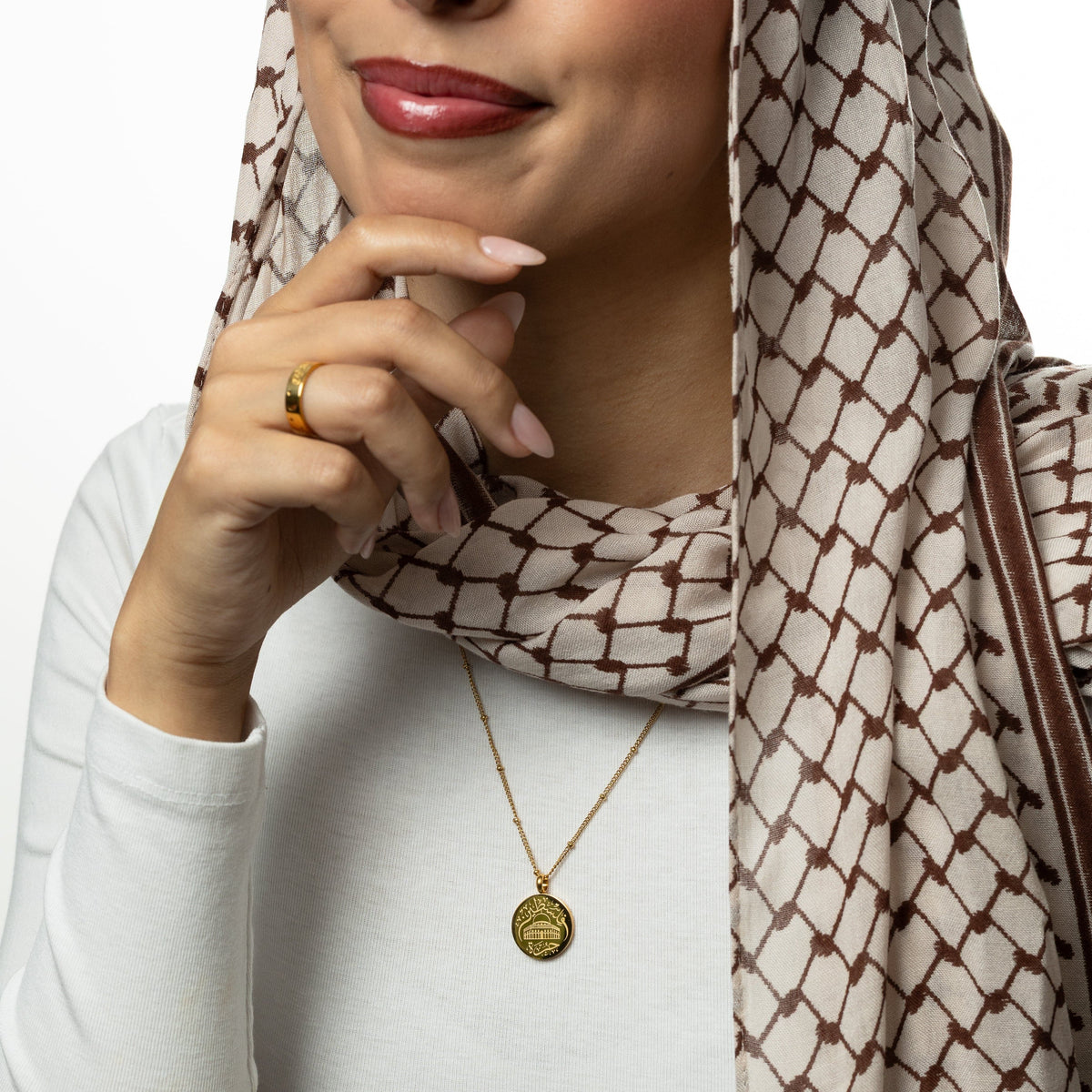 Woman wearing a keffiyeh patterned scarf and gold Al-Aqsa ‘Free Palestine’ Necklace on a white background