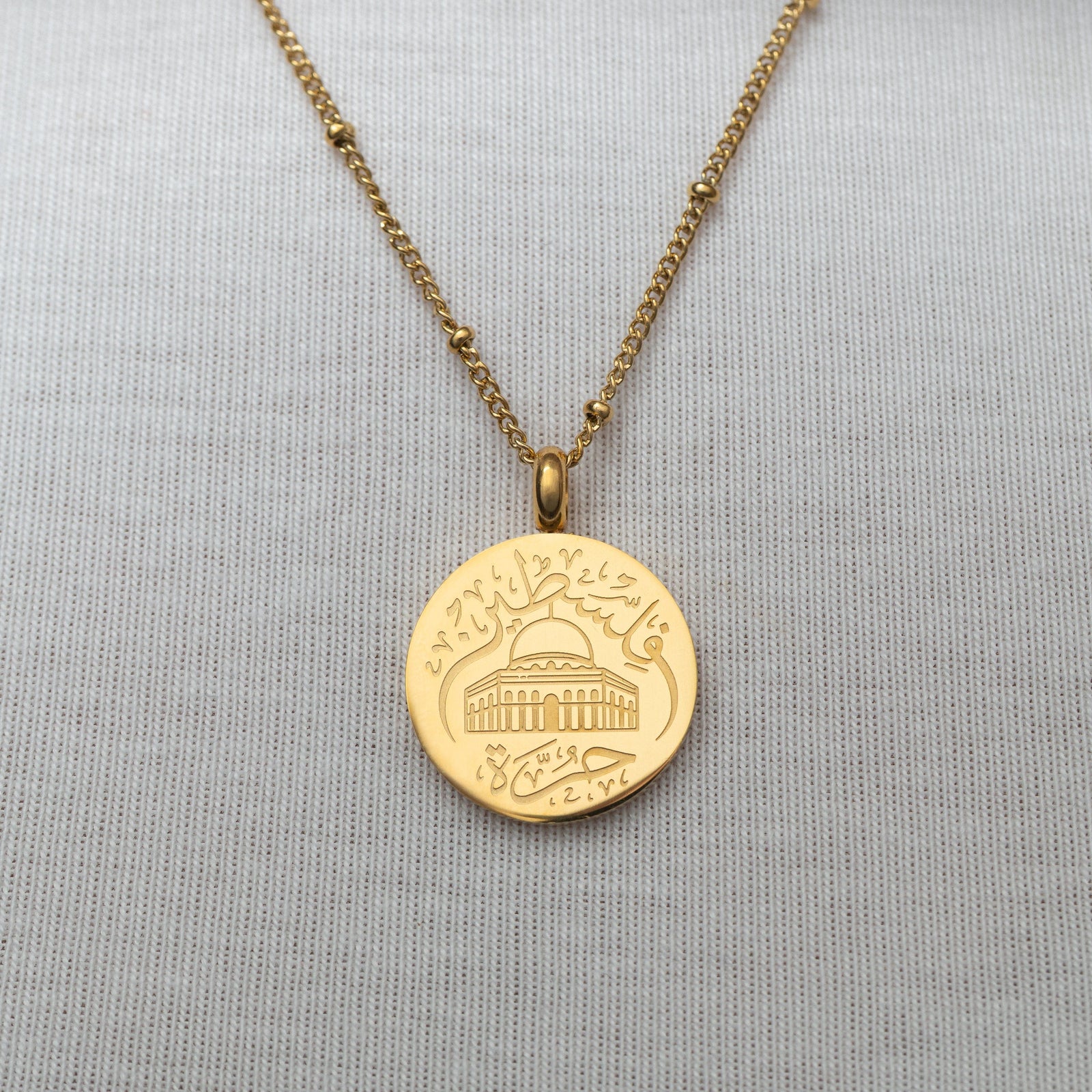 Gold Al-Aqsa ‘Free Palestine’ Necklace on a gray fabric background