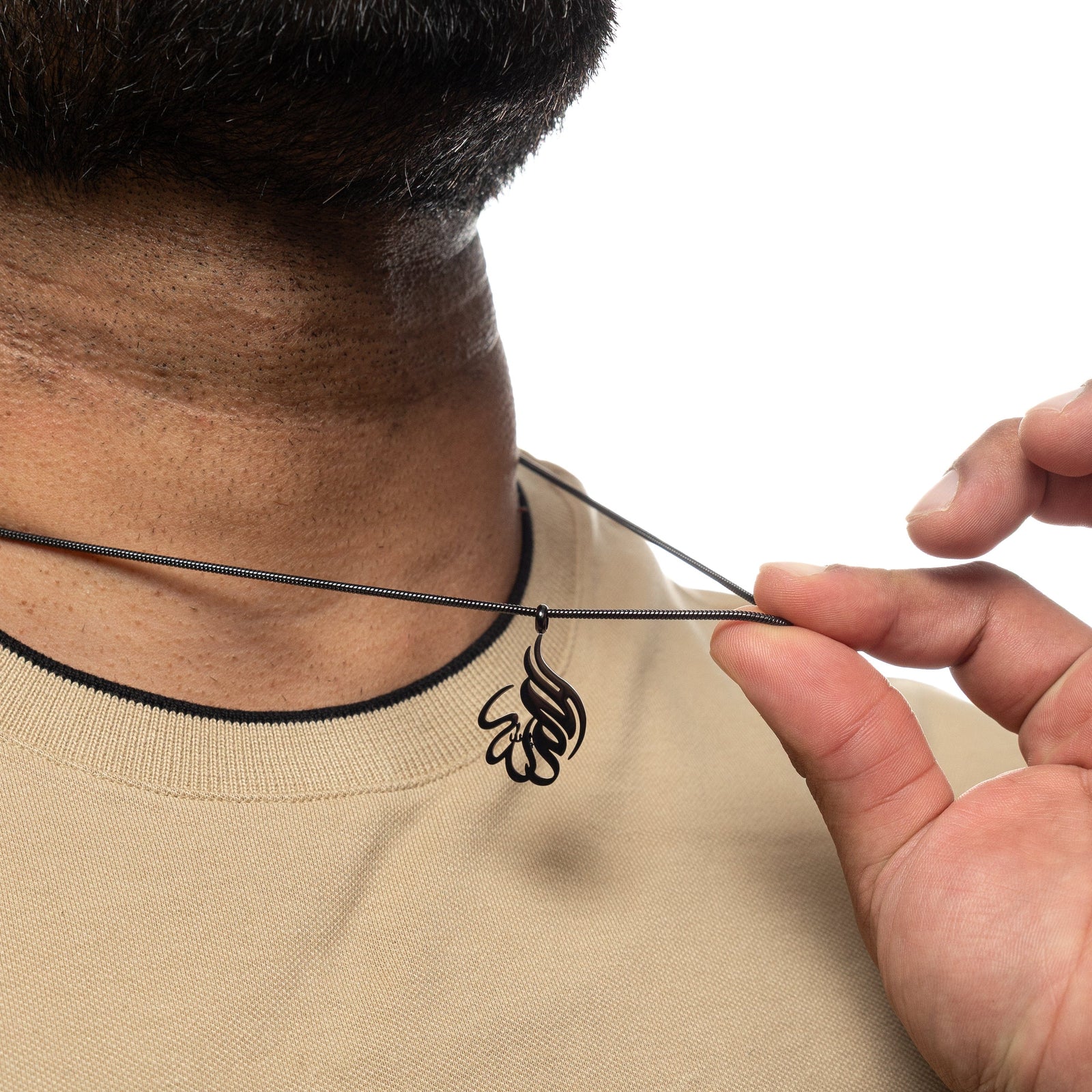 Man holding up a black 'Alhamdulillah' calligraphy necklace around his neck.