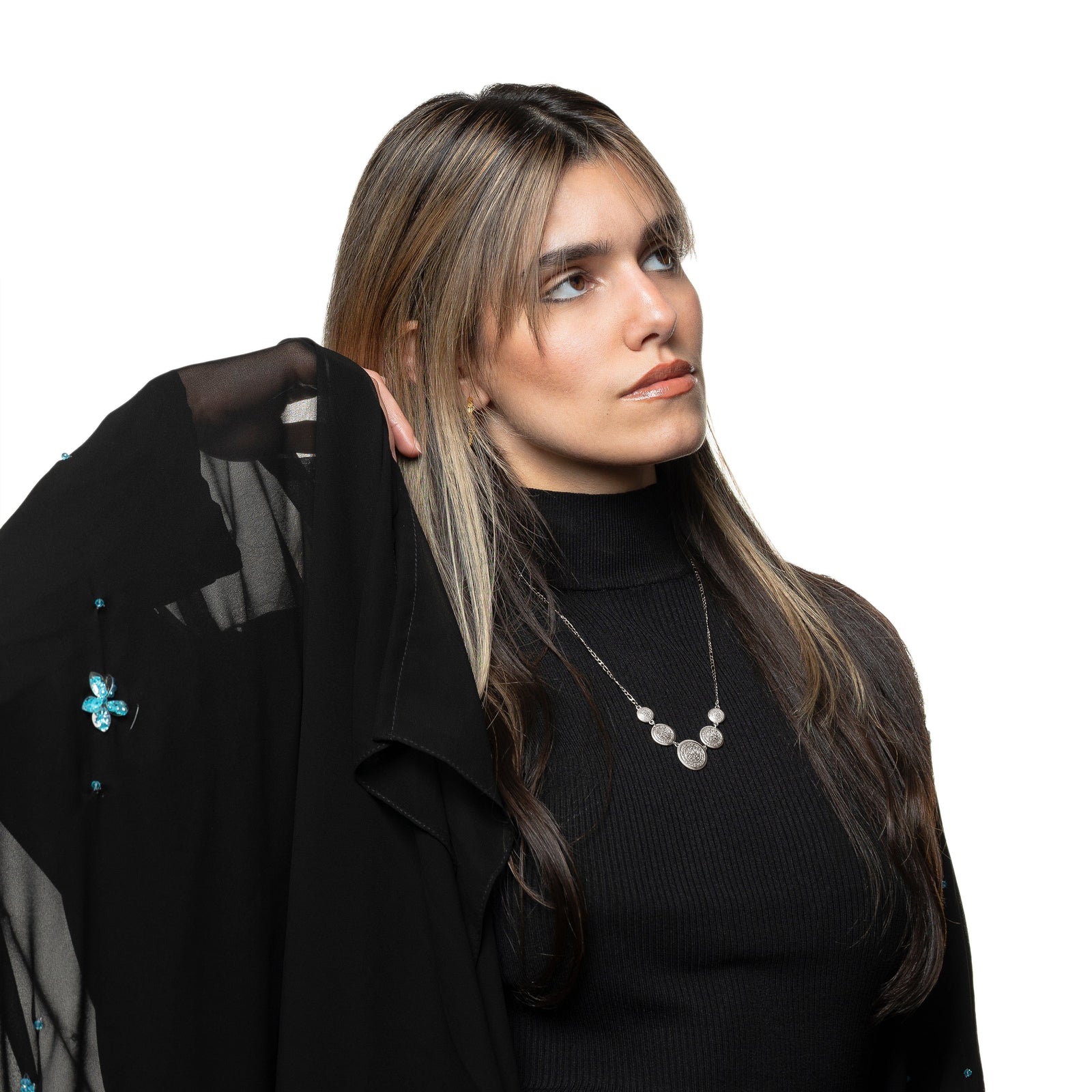 Photo of the model looking away from the camera, touching their hair with their right hand. The model is wearing the silver Alhamdulillah Coin Necklace.
