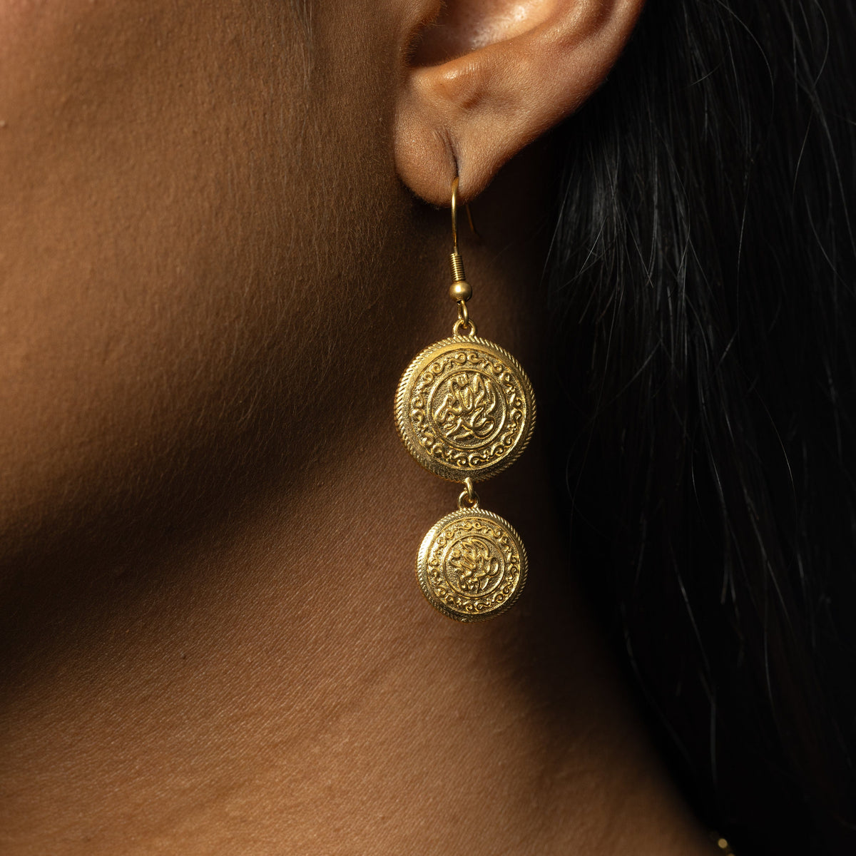Close up of the gold Alhamdulillah Coin Earring as worn by the model on their left ear.