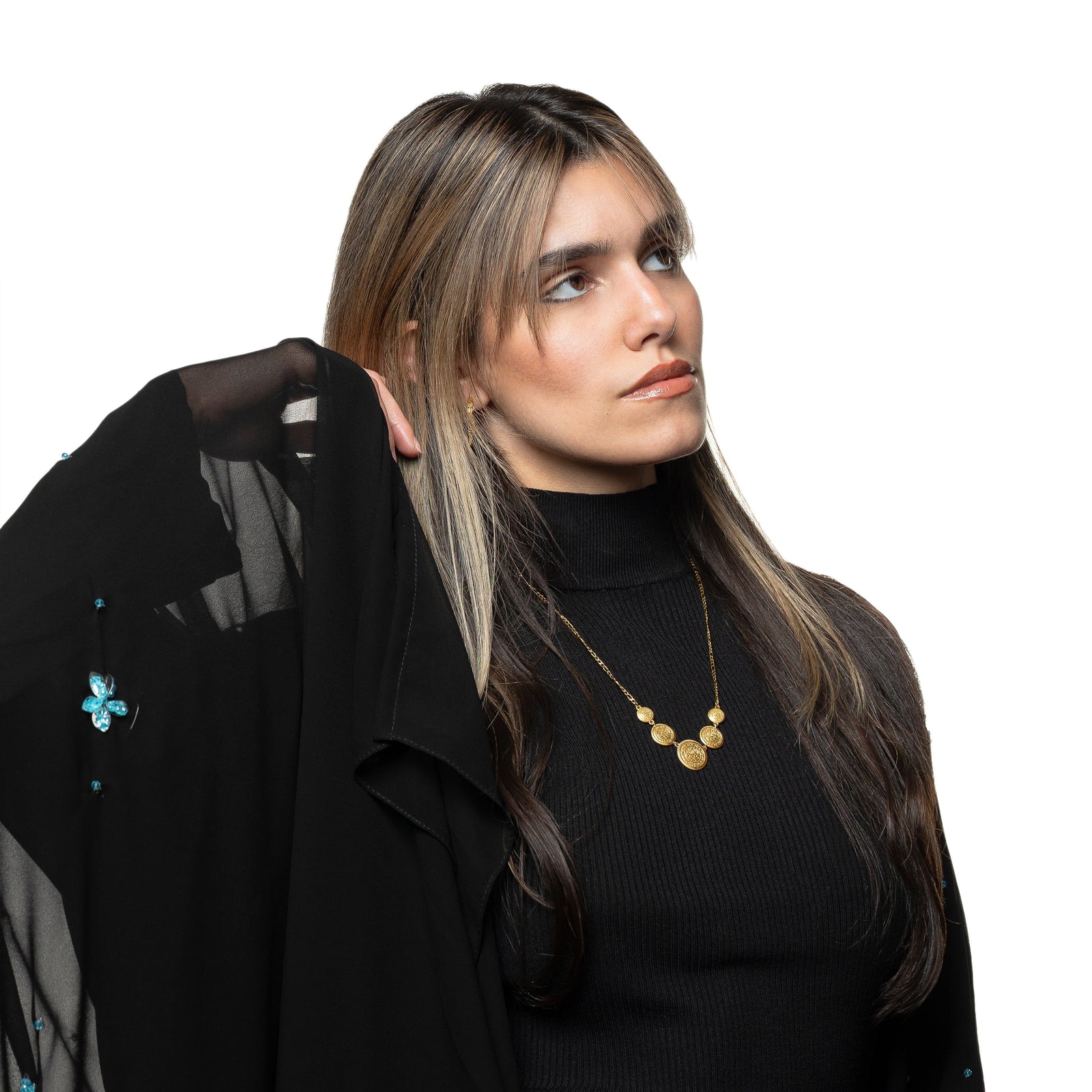 Photo of the model looking away from the camera, touching their hair with their right hand. The model is wearing the gold Alhamdulillah Coin Necklace.