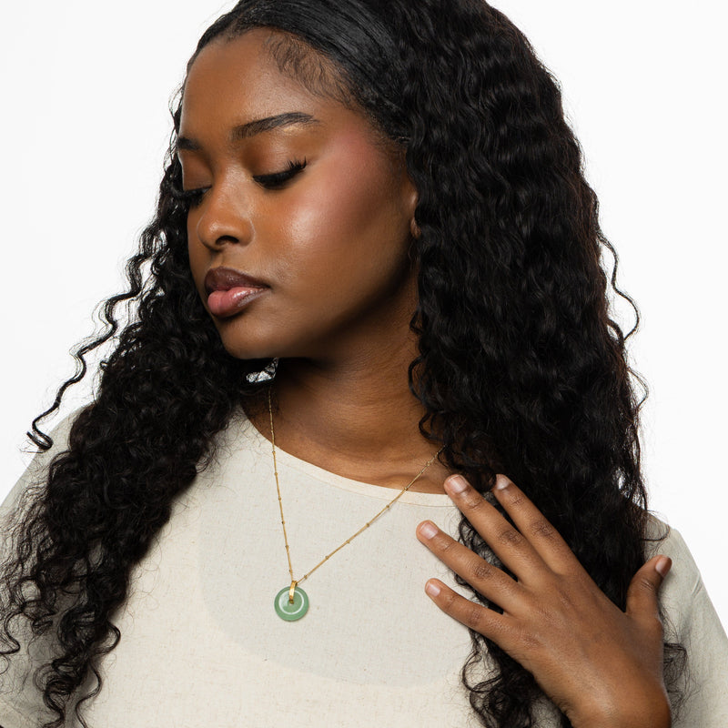 Woman wearing the green aventurine pendant necklace styled over a cream-colored top pimage_ hand resting near the collarbone.