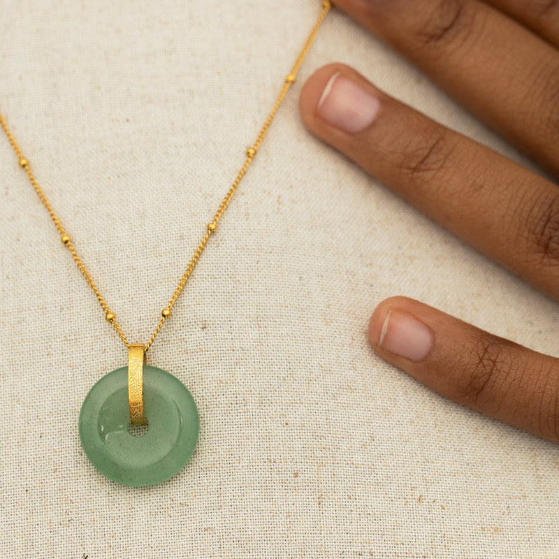 Necklace close-up on fabric pimage_ with the green aventurine stone pendant centered on a delicate gold chain with beaded accents.