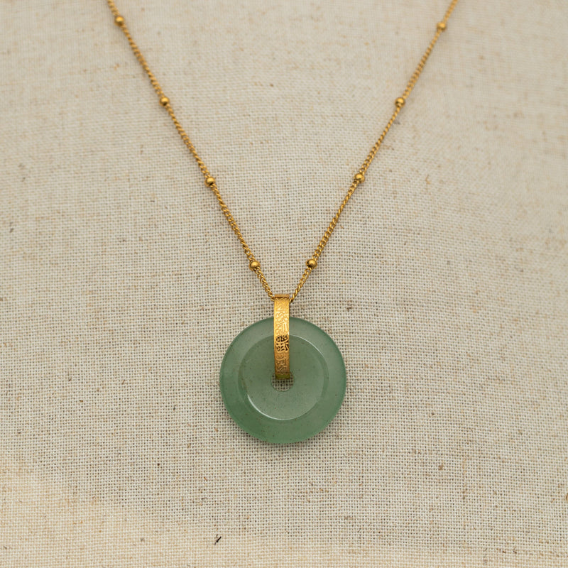 Necklace close-up on fabric pimage_ with the green aventurine stone pendant centered on a gold chain with beaded accents.