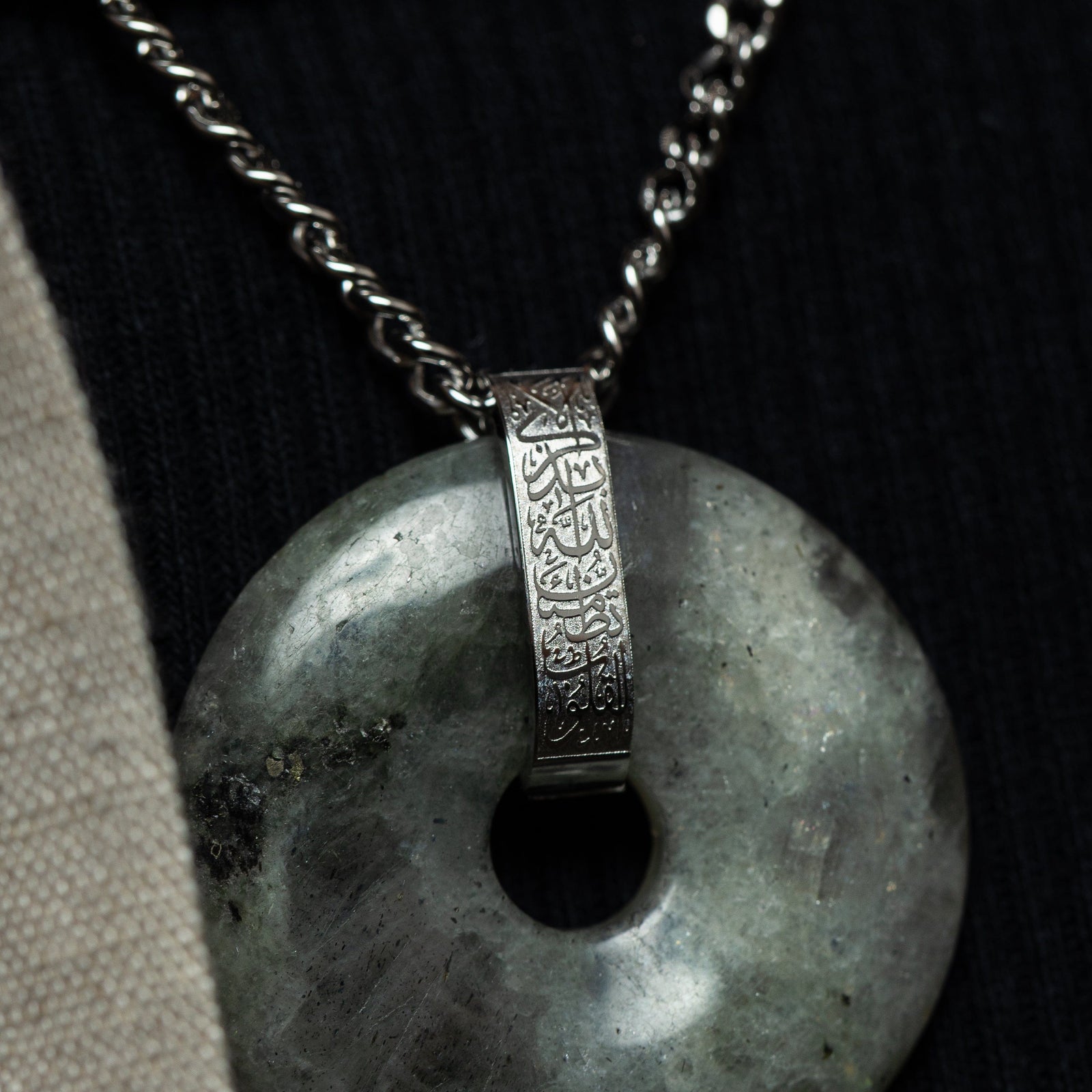 Close-up of the labradorite stone pendant with natural gray-green marbling, attached to a silver bail engraved in Arabic calligraphy.