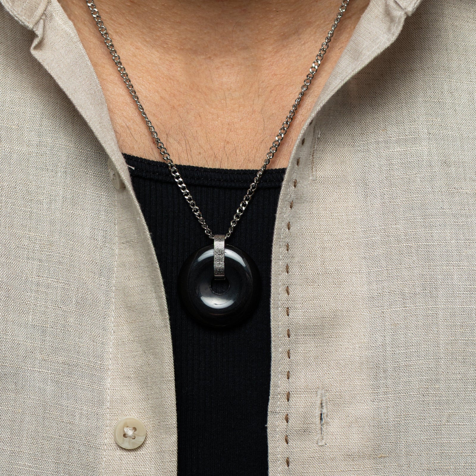 Chest-level view of the necklace resting over a black shirt, styled with a beige button-down layered on top.
