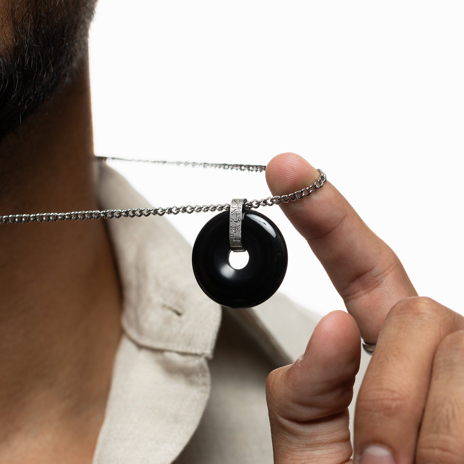 Close-up of a man holding forward the black onyx stone pendant with silver engraved bail.