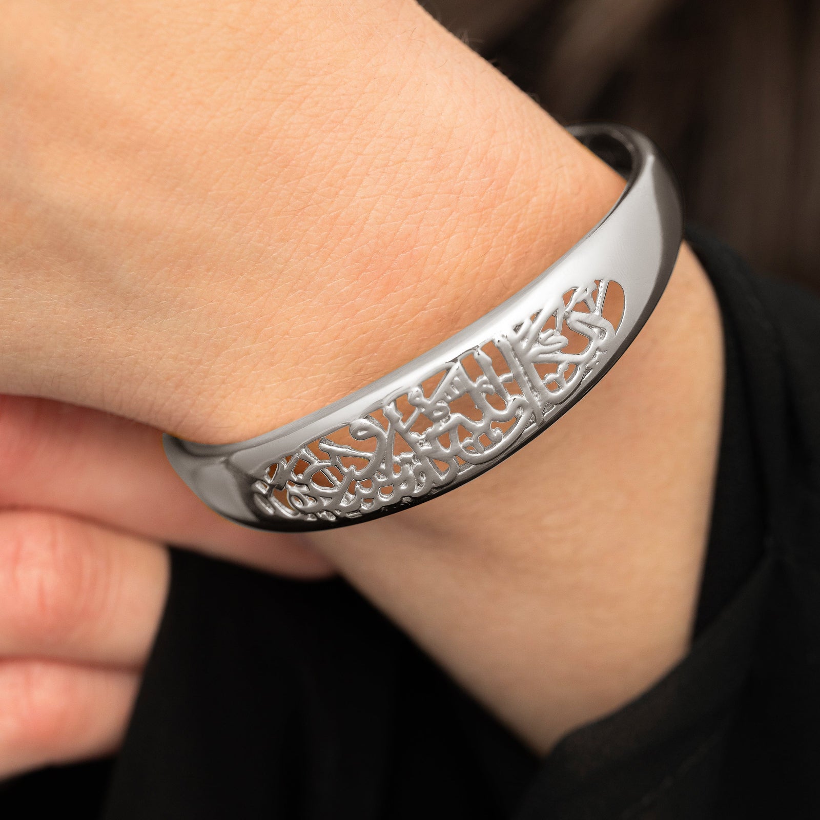 Close up of the silver "Allah does not burden a soul beyond what it can bear" Openwork Bangle worn by the model.