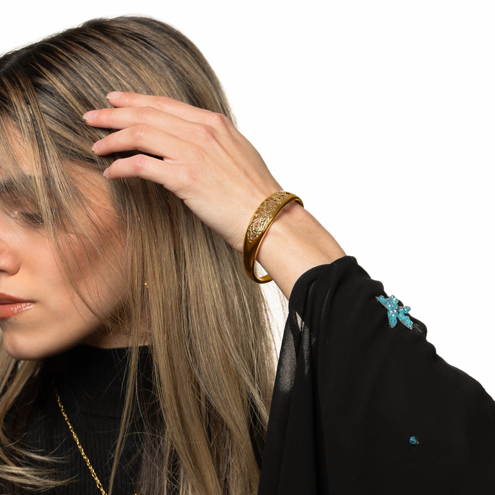 Model is touching their hair with their left hand. Model is wearing the gold "Allah does not burden a soul beyond what it can bear" Openwork Bangle on their left hand.