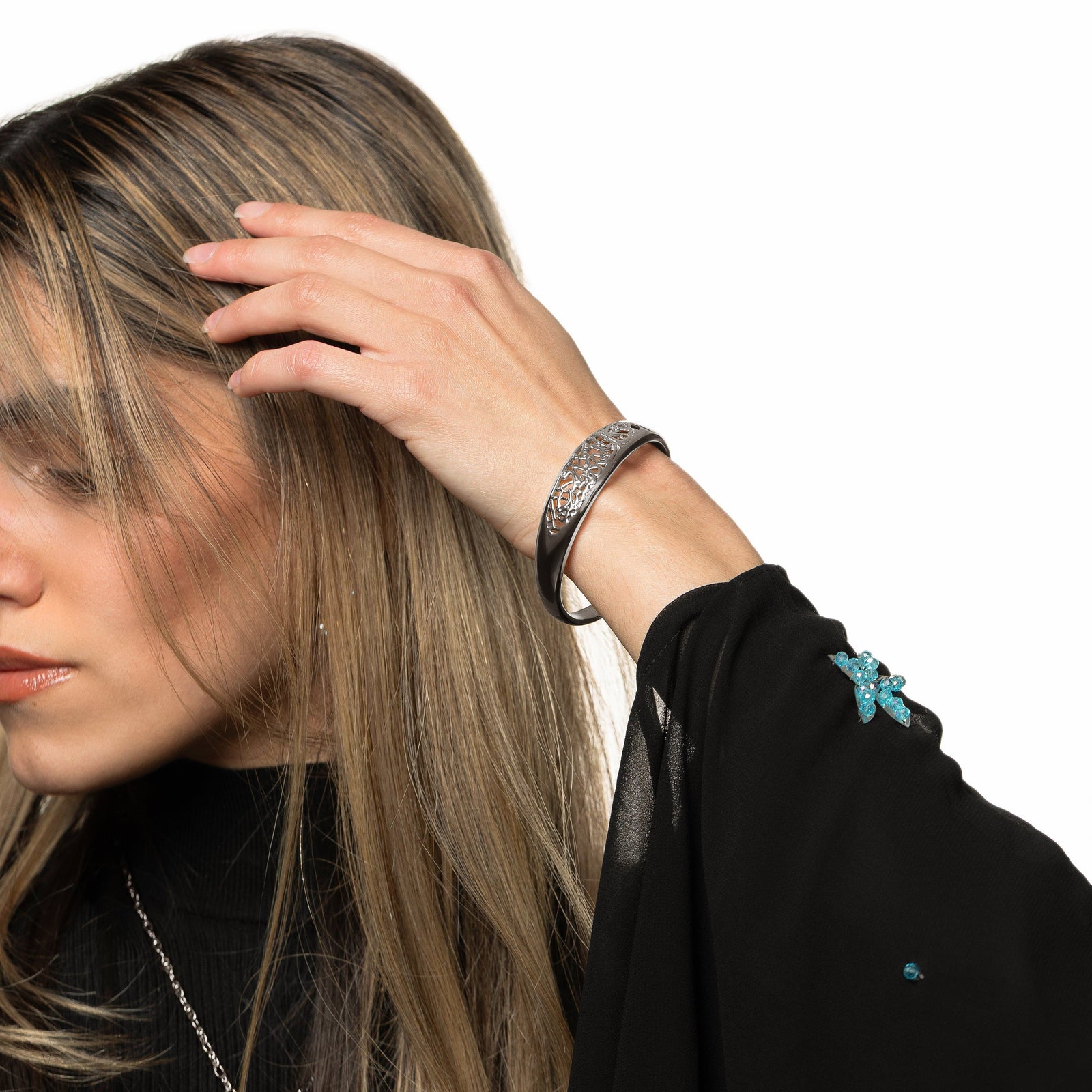 Model is touching their hair with their left hand. Model is wearing the silver "Allah does not burden a soul beyond what it can bear" Openwork Bangle on their left hand.