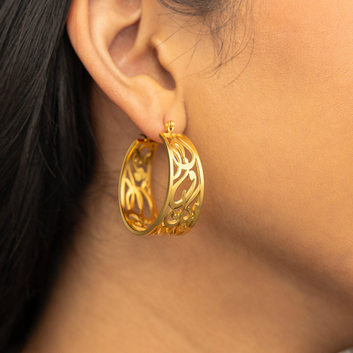 Close-up of the gold “Allah does not burden a soul beyond what it can bear” Earrings, showing the open-cut Arabic calligraphy hoop.