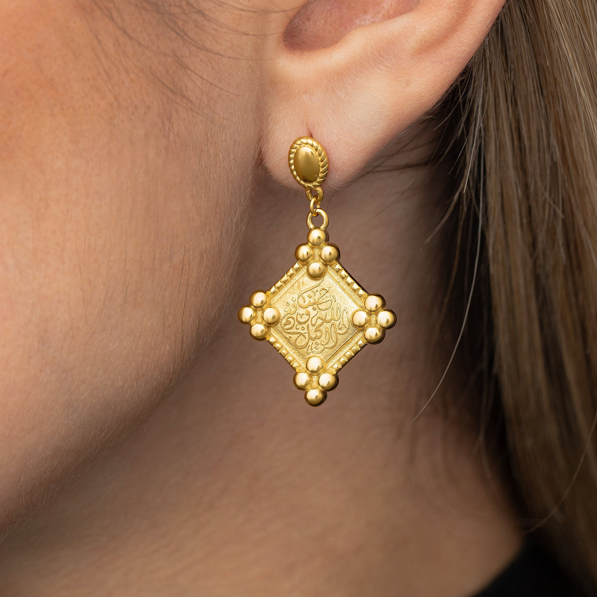 Close up of the gold "Allah is sufficient for us" Plaque Earring as worn by the model on their left ear.