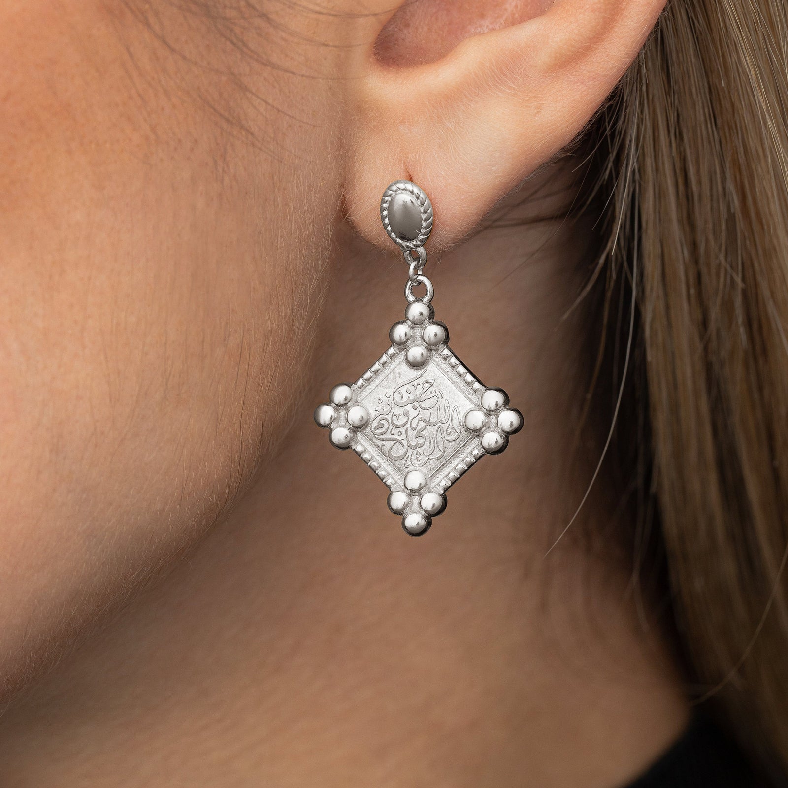 Close up of the silver "Allah is sufficient for us" Plaque Earring as worn by the model on their left ear.