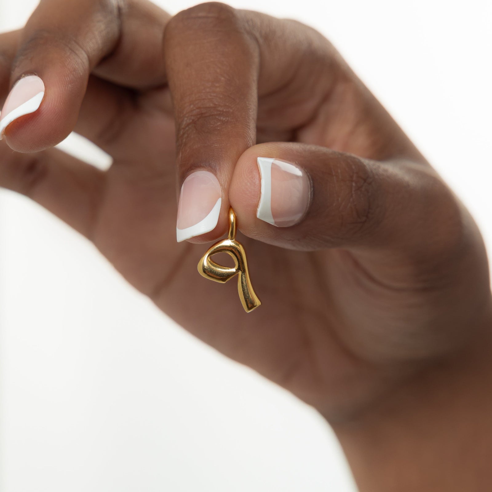 Close-up of the gold-plated Arabic number charm "٩" (9) on a shimmering pearl background.
