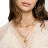 Woman wearing an 18k gold plated layered necklace with a poppy flower pendant and pale green tube beads, paired with drop earrings.