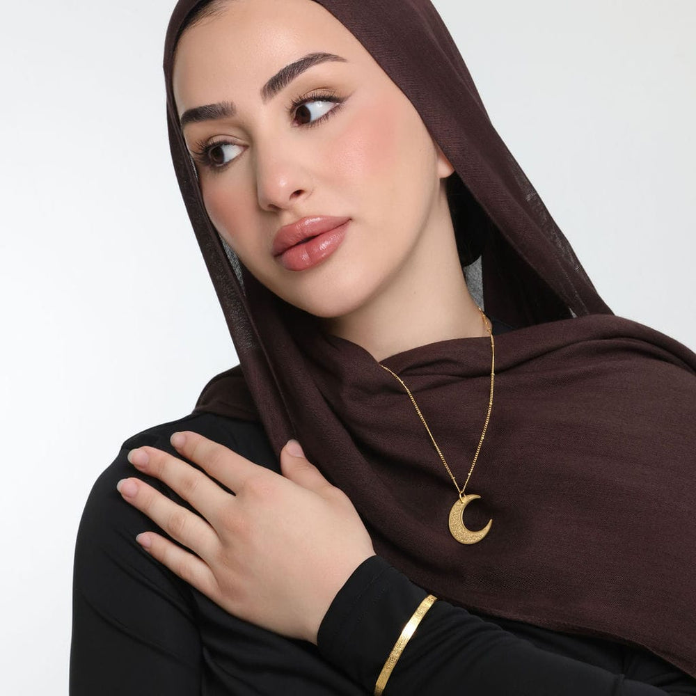 Photo of the model looking away from the camera with their left hand resting near their right shoulder. The model is wearing the gold Ayatul Kursi Crescent Necklace.