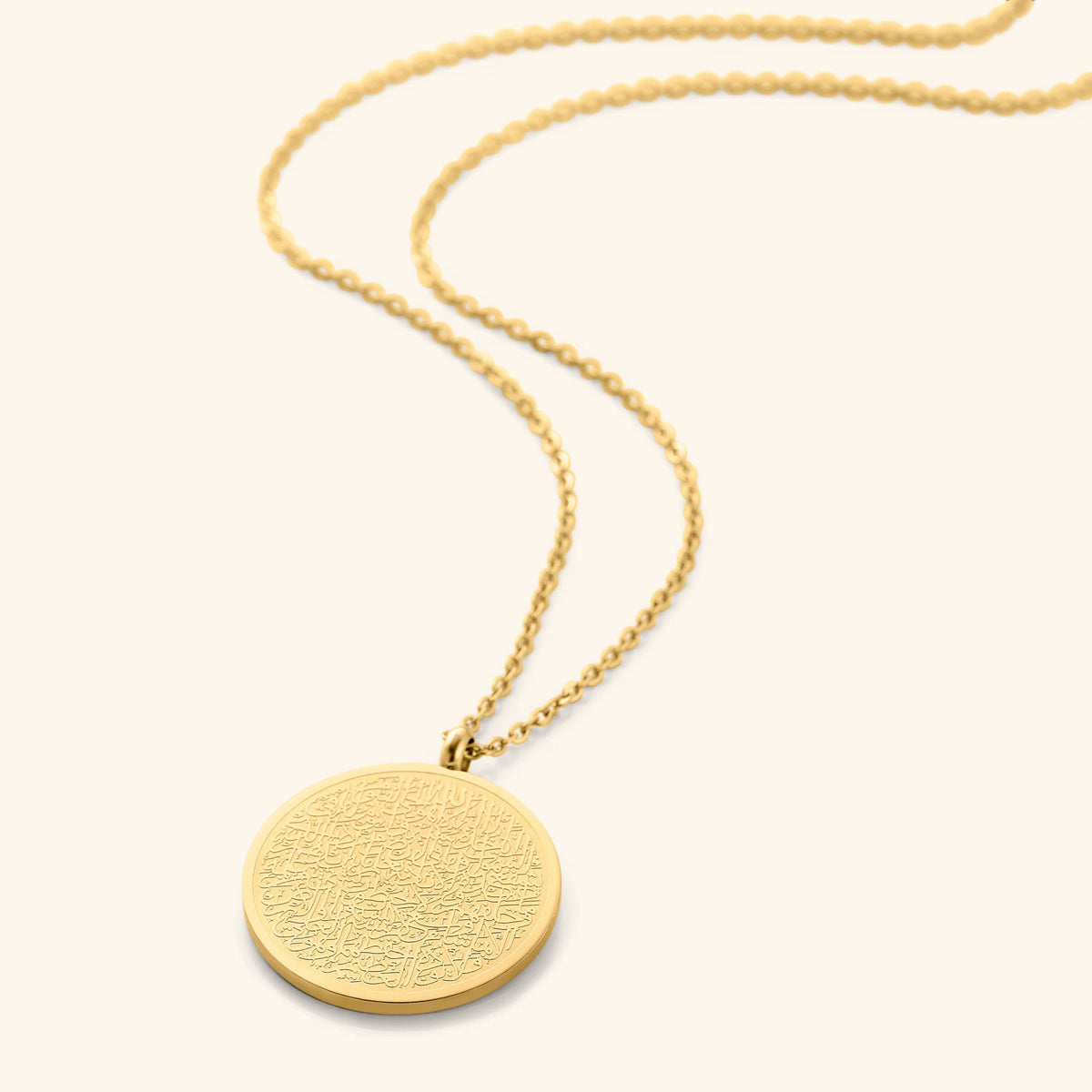 A gold necklace with a round pendant intricately inscribed with Arabic script. The chain is made of small gold beads. The necklace is displayed on a light beige background. Given the inscription and the product name "Ayatul Kursi Necklace," it is highly likely that the script is from the Quran, a central religious text in Islam, suggesting a possible religious significance for the wearer.