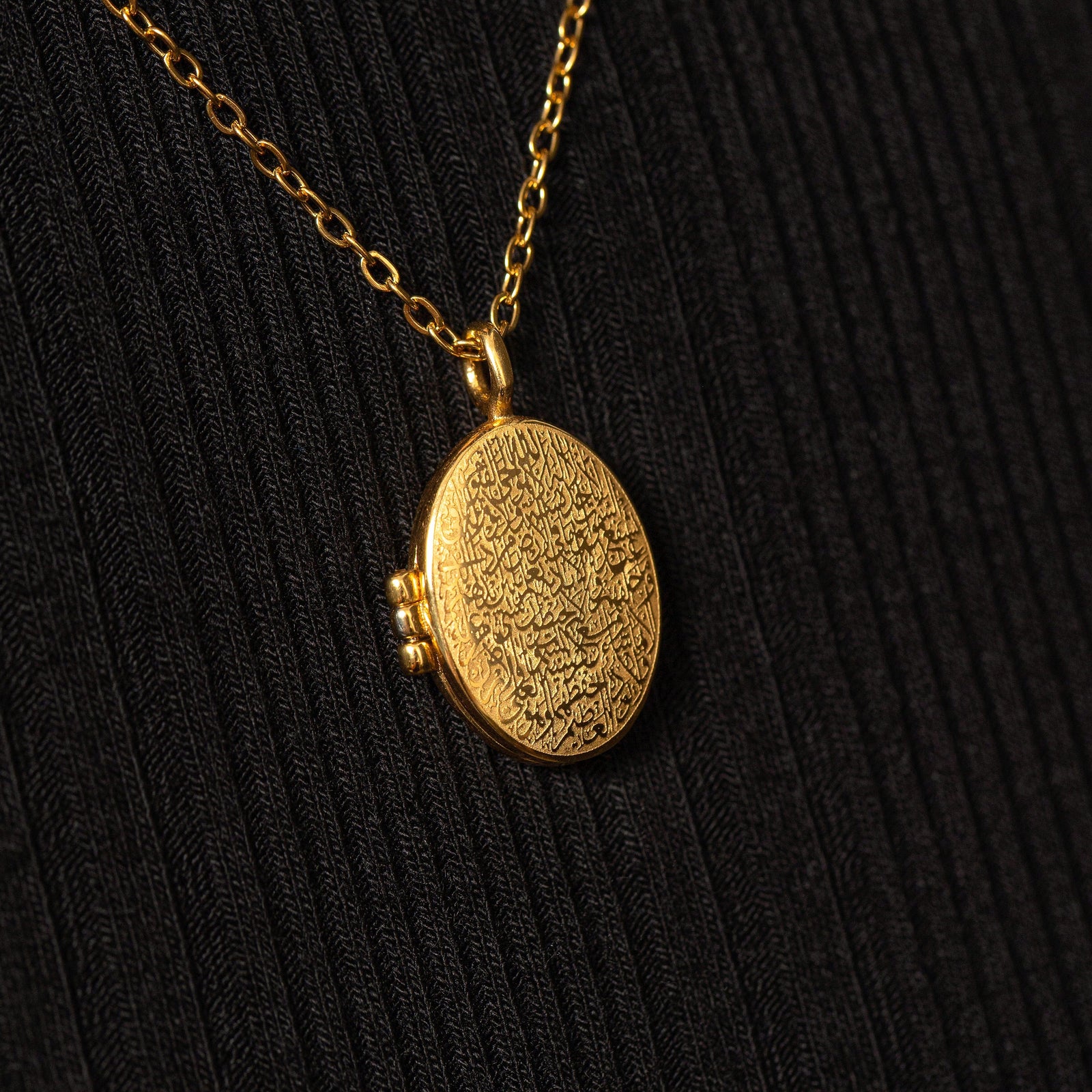 Gold Ayatul Kursi Locket with detailed engraved calligraphy, worn over a black ribbed top with the pendant centered in frame.