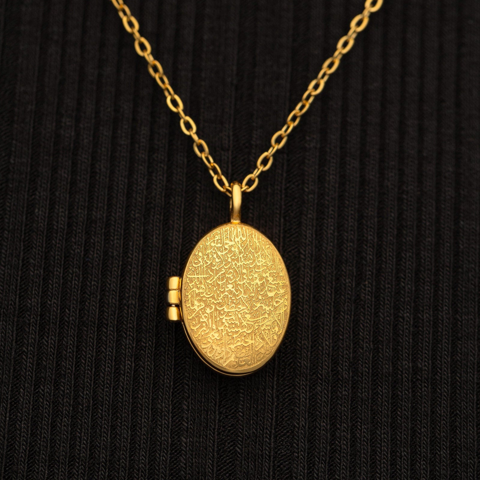 Gold Ayatul Kursi Locket with detailed engraved calligraphy, worn over a black ribbed top with the pendant centered in frame.