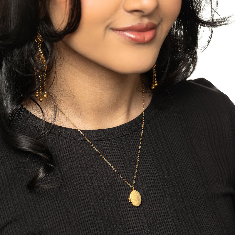 Gold Ayatul Kursi Locket worn over a black ribbed top pimage_ styled with gold earrings.