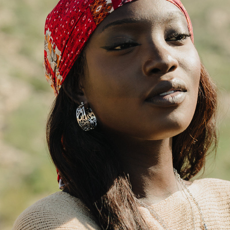 Woman wearing the “Allah does not burden a soul beyond what it can bear” Earrings in silver pimage_ styled with a red headscarf and photographed outdoors.