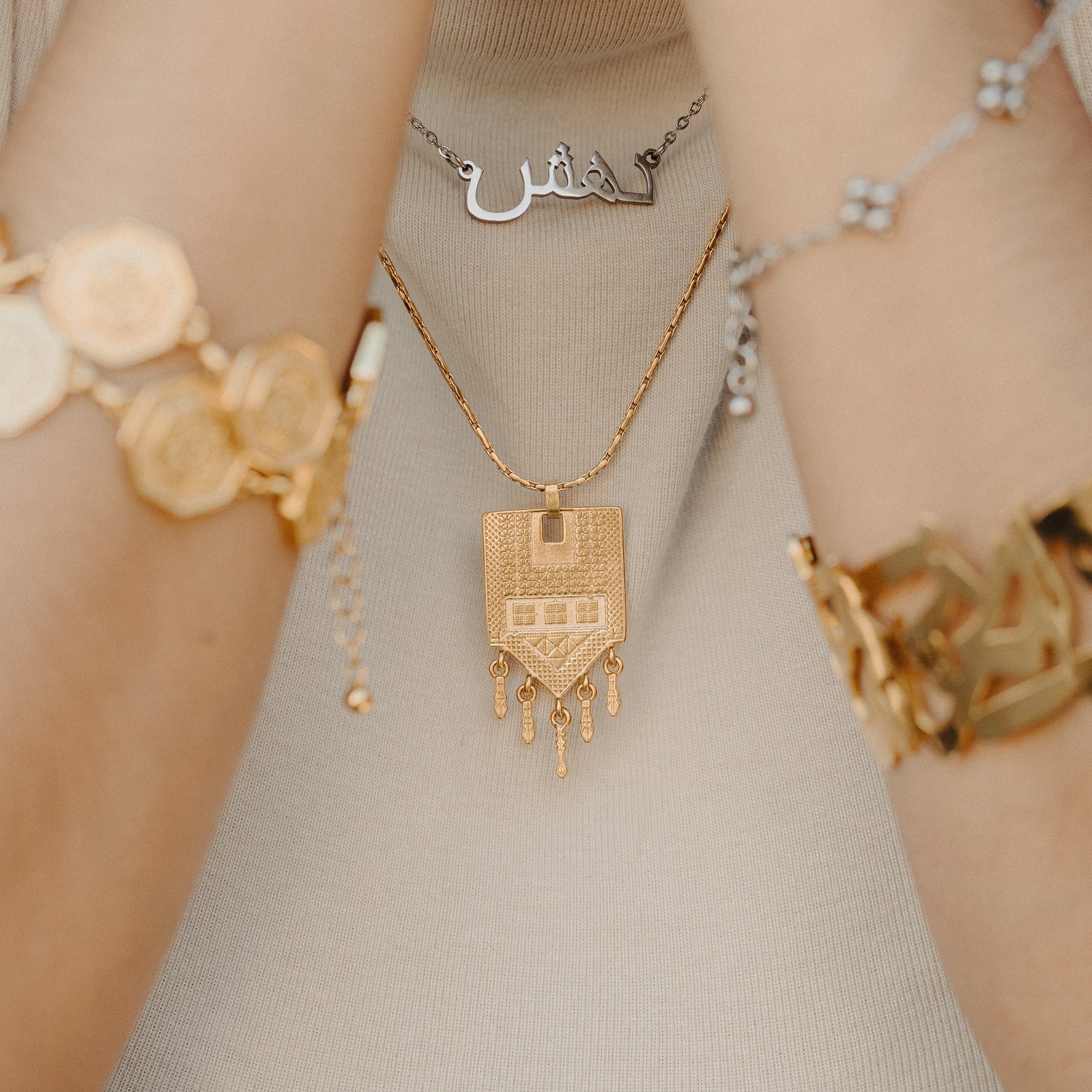 Raining Tatreez Necklace layered with another necklace, shown against a beige top.