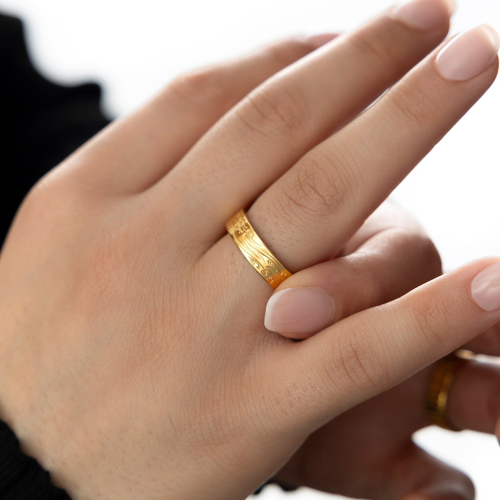 Close-up of hand wearing the gold “Be, and it is” ring with Arabic calligraphy, styled against a soft natural background.