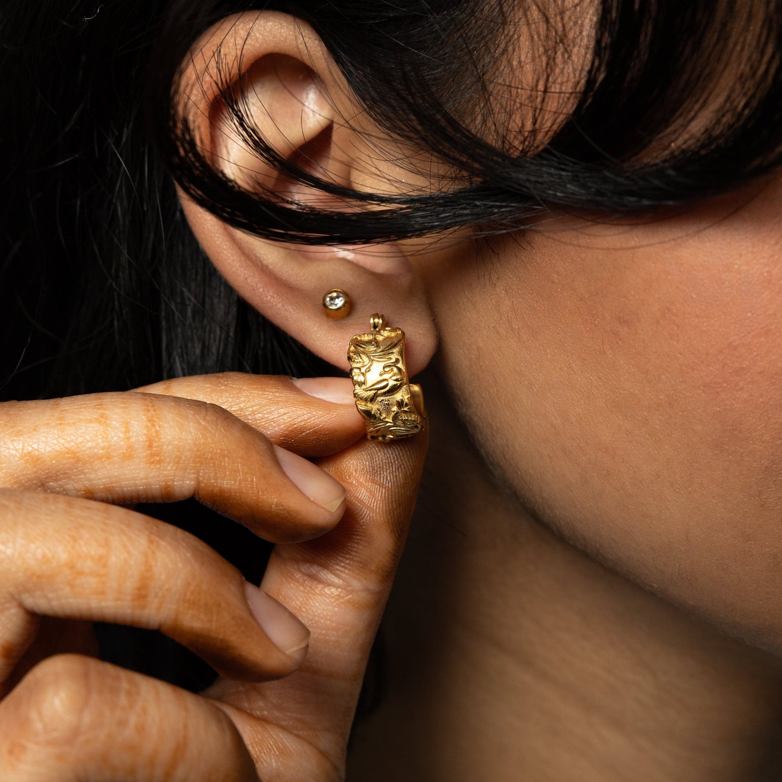 Model is touching the gold Bengal Bloom Earring worn on their right ear.