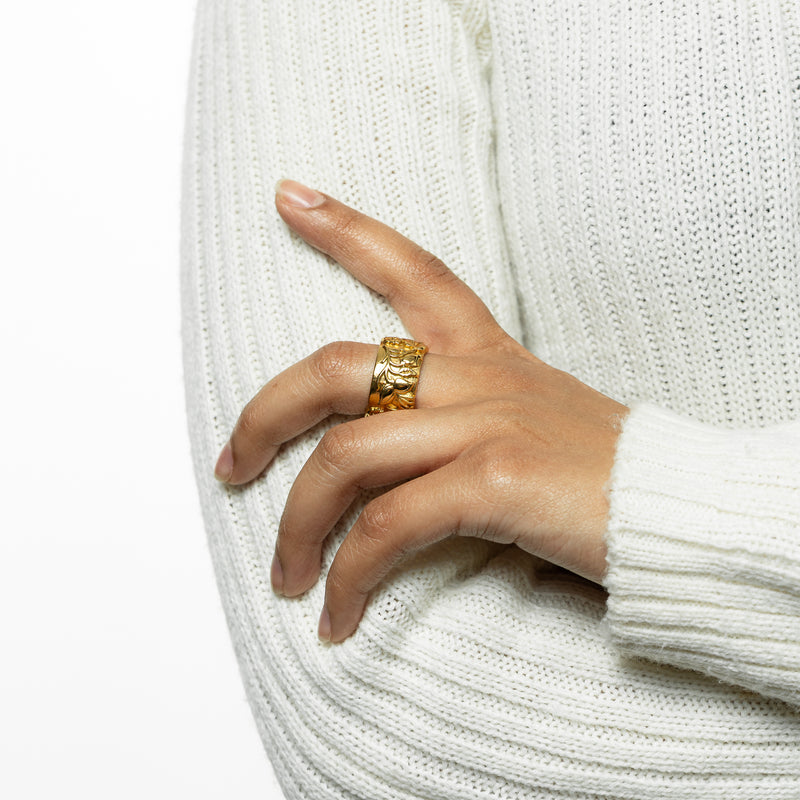 Woman wearing a gold Bengal Bloom Ring with ornate floral and peacock motifs pimage_ styled with a cream knit sweater and arm crossed over her body.