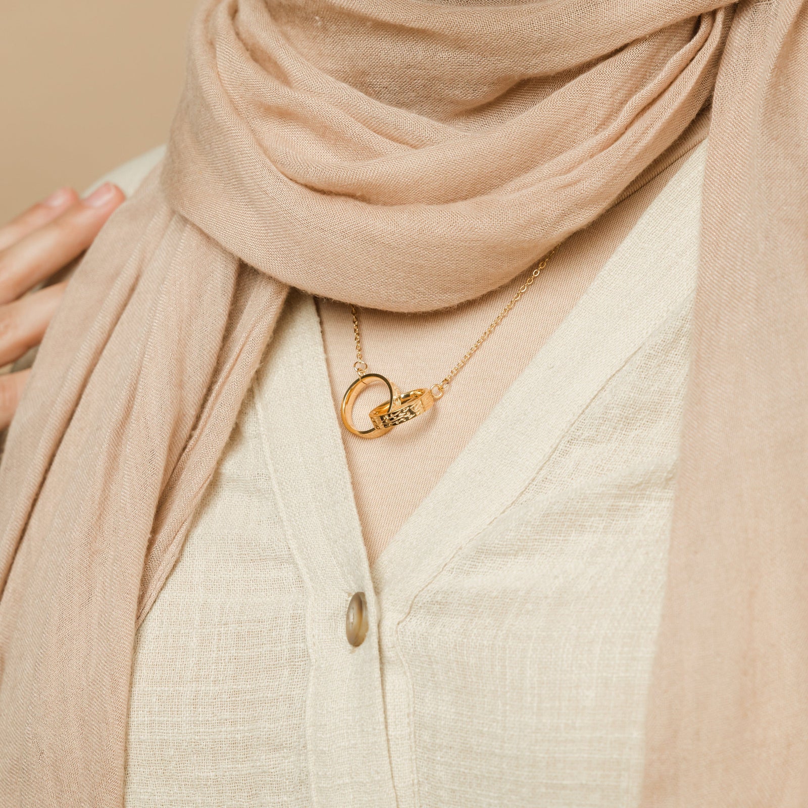 A close-up of the gold interlocked pendant showing fine Arabic calligraphy etched around the edge, emphasizing craftsmanship and meaning.