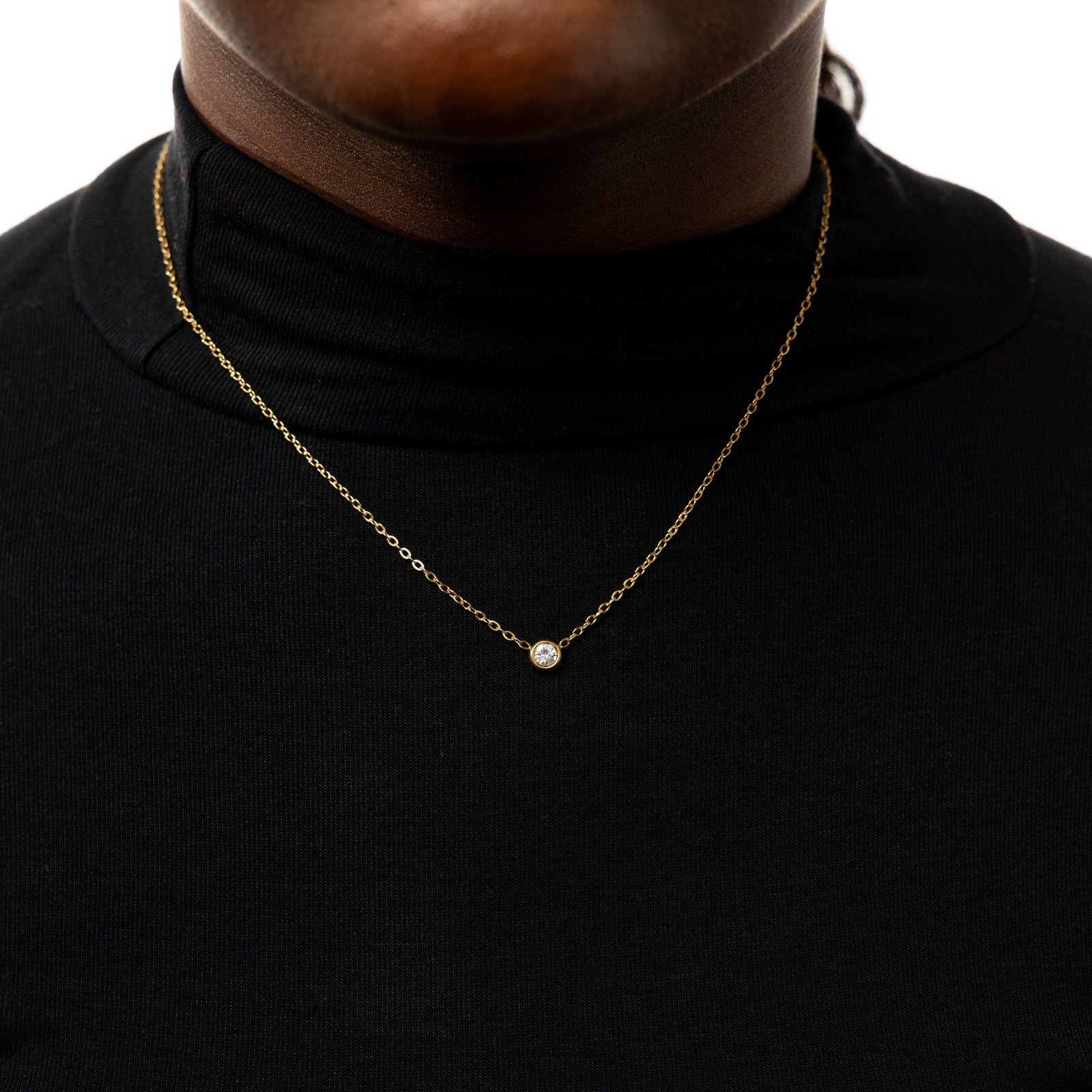 Close up of the gold Bezel Necklace against the black fabric of the model's clothing.