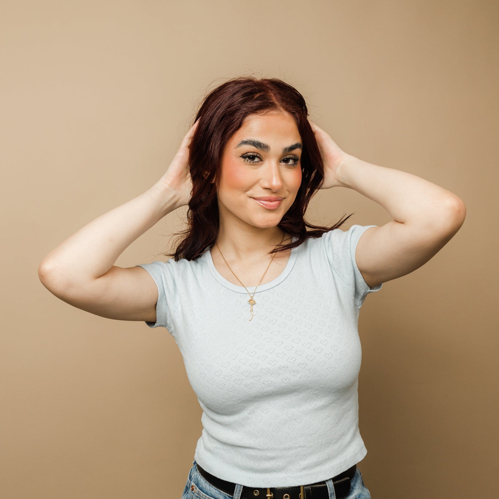 Photo of the model with both of their hands holding their head. They are wearing the gold Blooming Love Necklace.