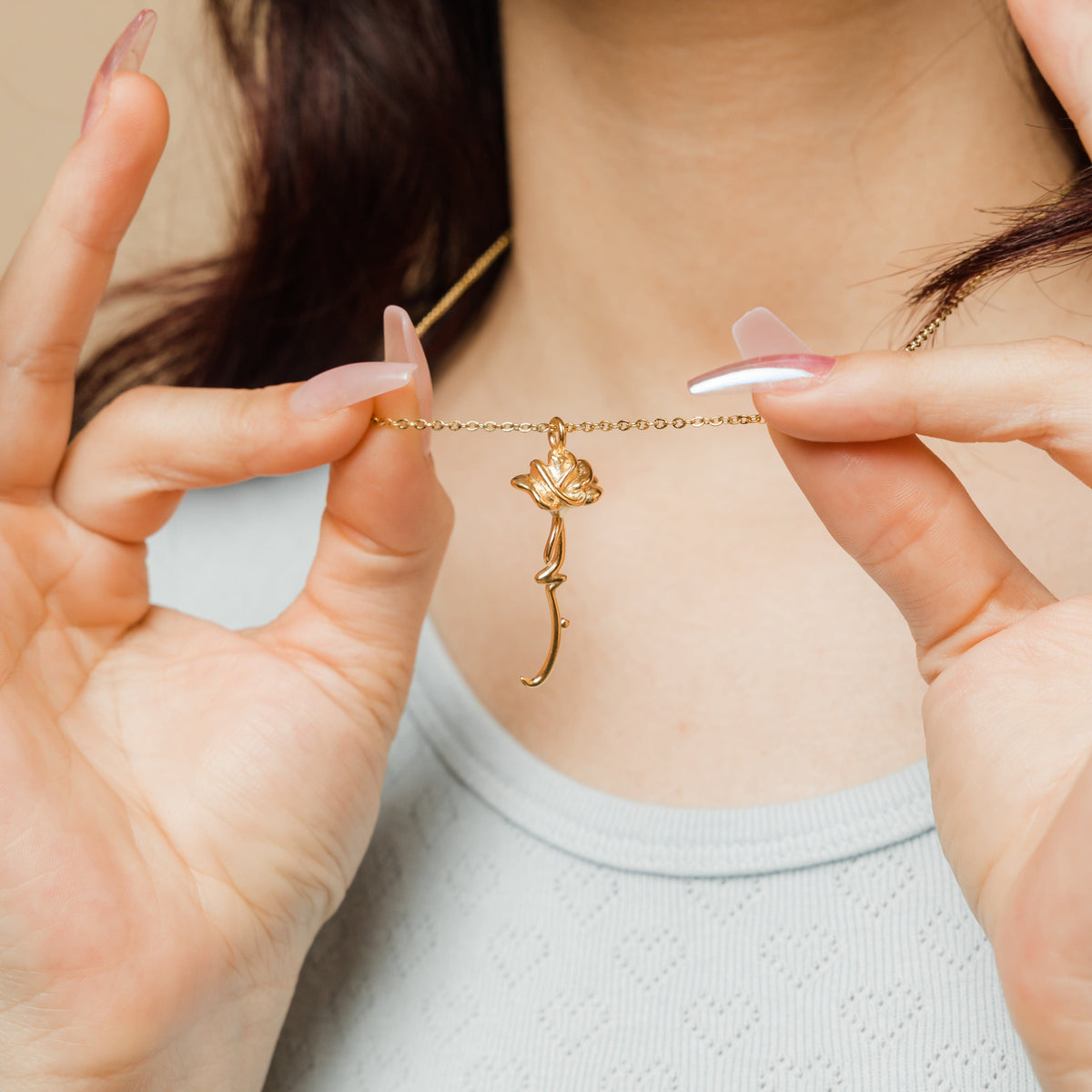 Photo of the model lifting the gold Blooming Love Necklace by its chain to showcase its gold pendant.