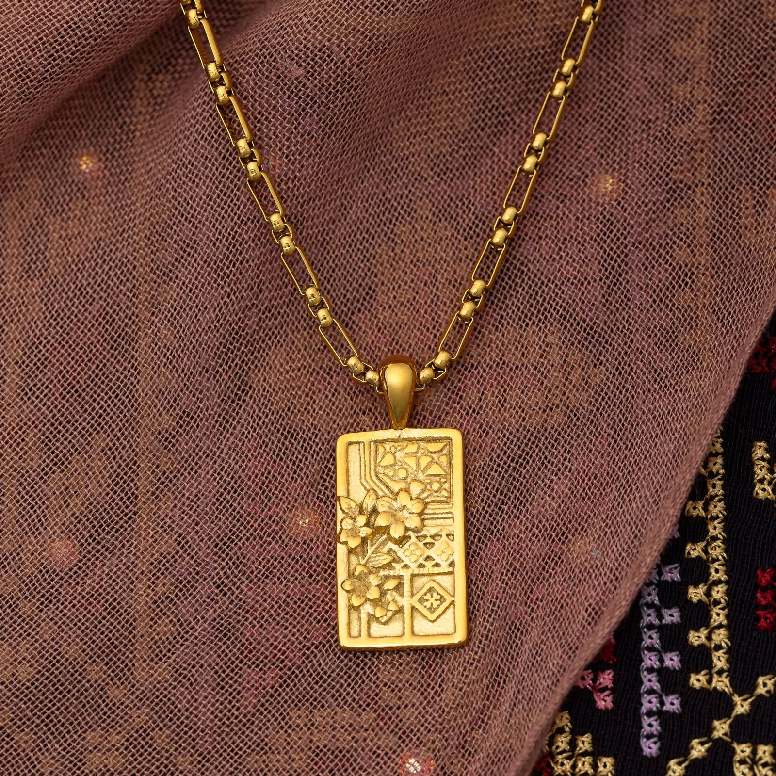 Close up photo of the gold rectangular pendant on a gold chain.