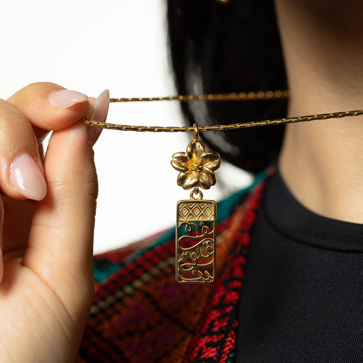 Close up photo of the model holding the gold chain of the Blooming in Our Hearts necklace to show the design of its pendant.