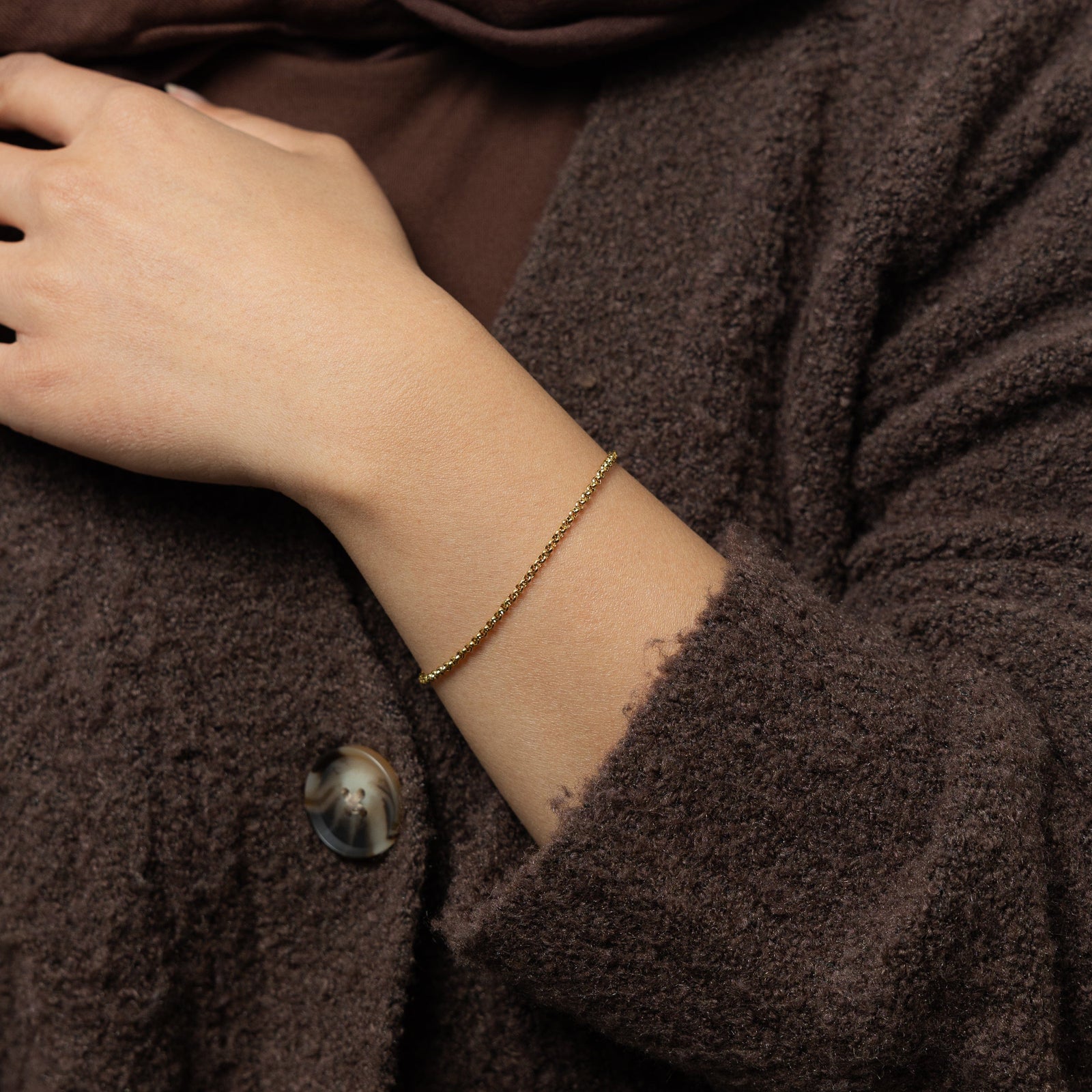 Photo of the model wearing the gold Micro Box Bracelet on their left wrist